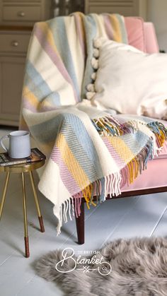 a chair with a blanket on top of it next to a table and some pillows