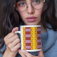 a woman wearing glasses holding a coffee mug in front of her face and looking at the camera