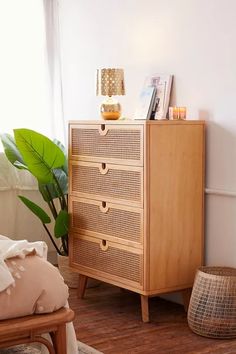 a wooden cabinet with drawers and baskets on the floor next to a plant in a living room