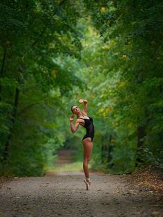 a woman running down a dirt road in the middle of a forest with lots of trees