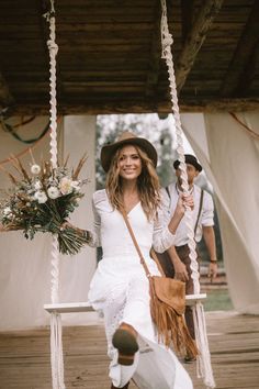 a woman sitting on a swing with flowers in her hand and a man standing next to her