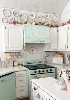 an old fashioned kitchen with white cabinets and green stove top oven in the center, surrounded by plates on the wall