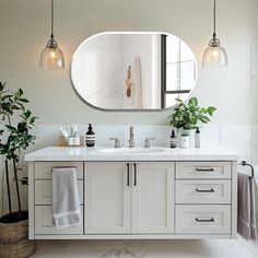 a bathroom with a large round mirror above the sink and two plants in front of it