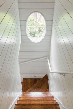 the inside of a house with white walls and wooden steps leading up to a round window