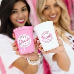 two women holding up pink and white cups