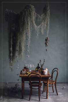 a dining table with two chairs and an arrangement of branches hanging from the ceiling above it