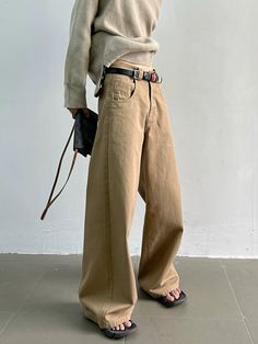 a man standing in front of a white wall with his hands on his hips and wearing brown pants