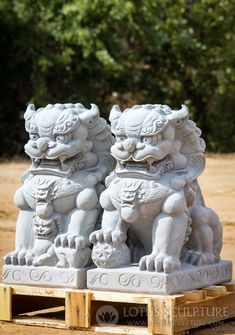 two white foo foo statues sitting next to each other on top of a wooden pallet