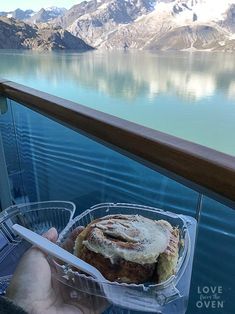 a person holding a plastic container with food in it on a balcony overlooking water and mountains