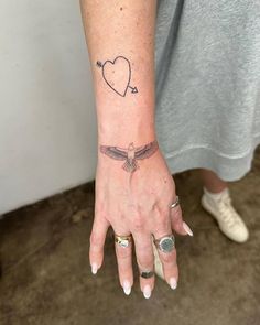 a woman's hand with a heart and an arrow tattoo on her left wrist