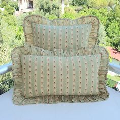 two pillows sitting on top of a white table next to a window with trees in the background