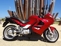 a red motorcycle is parked in front of some wooden poles and fenced in area