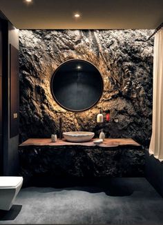 a black and white bathroom with a round mirror on the stone wall above the sink