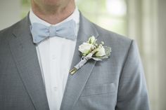 a man in a gray suit with a blue bow tie and boutonniere