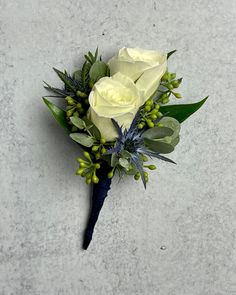 a boutonniere with white roses and greenery on a concrete surface,