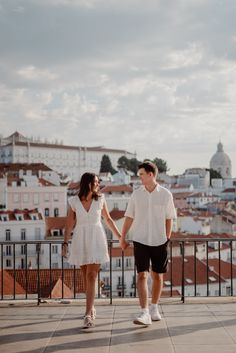 a man and woman holding hands while standing next to each other on top of a building