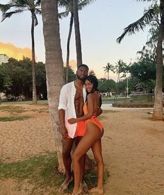 a man and woman standing next to each other in front of palm trees on the beach