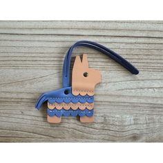 a blue and brown horse shaped ornament hanging from a wooden table with a leather cord