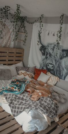 an unmade bed with pillows and blankets on it in front of a cow tapestry