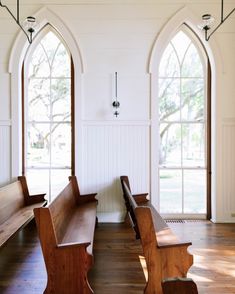 two wooden benches sitting in front of three arched windows with wood flooring and white walls