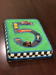 a birthday cake that is shaped like a race track with cars on it and the number five