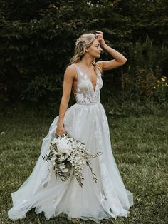 a woman standing in the grass holding a bouquet and wearing a wedding dress with an open back