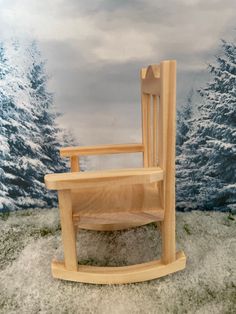 a wooden rocking chair sitting on top of snow covered ground next to a forest scene