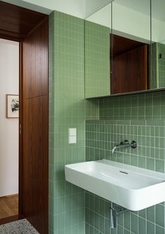 a white sink sitting under a bathroom mirror next to a green tiled wall and floor