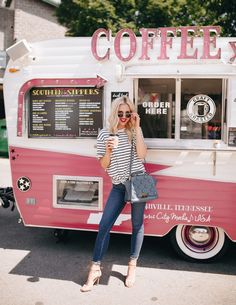 a woman standing in front of a pink and white food truck with the word coffee on it