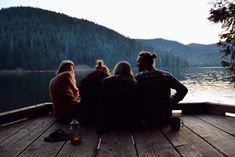 four people sitting on a dock looking at the water