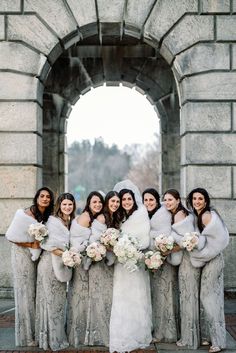 a group of women standing next to each other in front of a stone arch holding bouquets