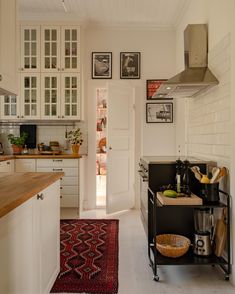 a kitchen with white cabinets and wooden counter tops next to a red rug on the floor