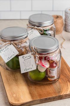 three mason jars filled with pickles on top of a wooden cutting board next to a jar of jam