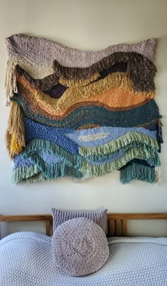 a bed topped with a pile of blankets next to a wall hanging on the side of it