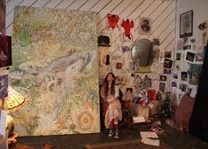 a woman standing next to a painting in a room filled with pictures and other items