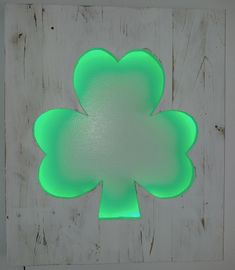 a four leaf clover shaped neon green object on a white wall with wood planks