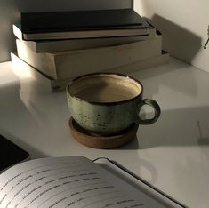 an open book sitting on top of a desk next to a coffee cup and stack of books