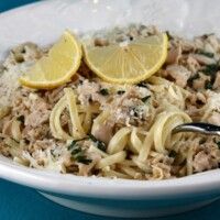 a white bowl filled with pasta, meat and lemons on top of a blue table