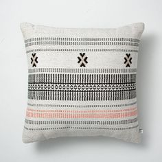 a white pillow with an orange and black design on the front, sitting against a wall