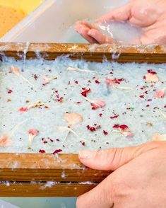 two hands reaching for something in a wooden box filled with water and flowers on it