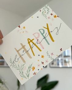 someone holding up a happy birthday card with flowers and greenery on the front side