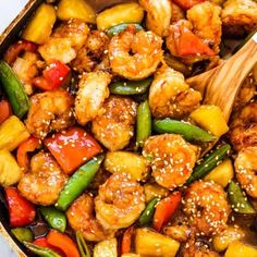 chicken and pineapple stir fry in a skillet with a wooden spoon on the side