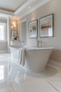 a large white bath tub sitting in a bathroom next to two framed pictures on the wall