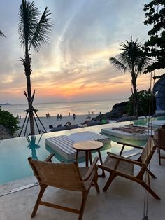 some chairs and tables near a swimming pool with people on the beach in the background