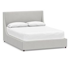 an upholstered bed with white sheets and pillows