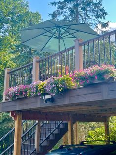 a deck with flowers and an umbrella over it in front of a car parked on the street