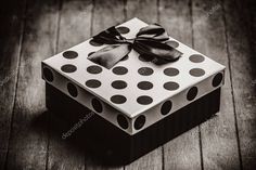 a black and white photo of a gift box with a bow on it, sitting on a wooden floor