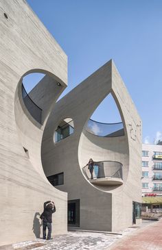 two people are standing in front of a building with large circular windows and curved concrete walls