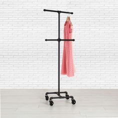 a pink dress hanging on a rack in front of a white brick wall with black wheels