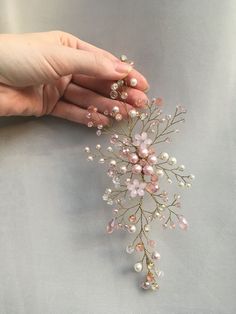 a woman's hand is holding a pink and white flower hair comb with pearls on it